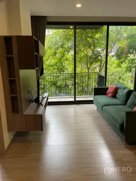 公寓 出租在Watthana, Bangkok - 明亮客厅面向大面积推拉玻璃门，阳台俯瞰葱郁树景。