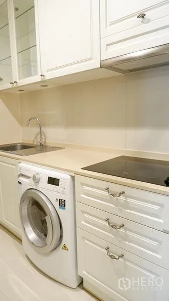 Condominium for rent in Watthana, Bangkok - Kitchen counter with induction hob, sink, and front-load washing machine.