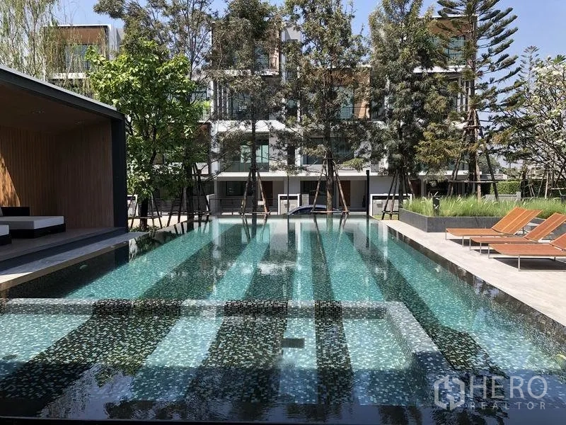 Townhouse for rent or sale in Saphan Sung, Bangkok - Shared lap pool with sun loungers and a pavilion amid landscaped gardens.