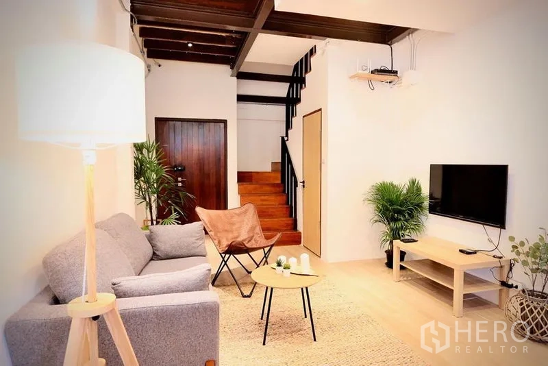 Office Space for rent in Sathon, Bangkok - Bright living area with gray sofa, TV console, wooden stairs, indoor plants and exposed ceiling beams.
