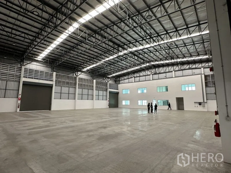 โรงงาน ให้เช่าในBang Sao Thong, Samut Prakan - ภายในคลังสินค้าโล่ง เพดานโค้งโครงเหล็ก พื้นคอนกรีตขัดมัน มีหน้าต่างออฟฟิศชั้นลอยและประตูม้วนขนาดใหญ่.