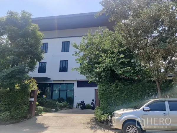 带办公室的家 出售 - 多层办公楼正面，车道与茂密树木环绕。