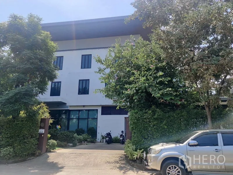 带办公室的家 出售 - 多层办公楼正面，车道与茂密树木环绕。