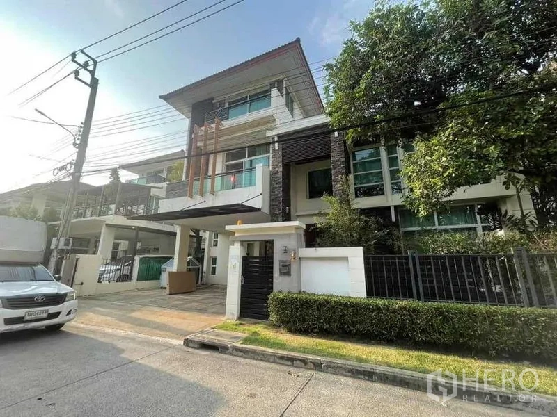 Detached House for rent or sale in Khan Na Yao, Bangkok - Modern three-storey detached house facade with gated entrance, carport and mature trees in an upscale estate.