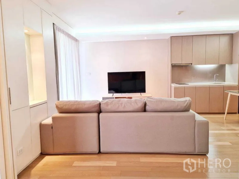 Condominium for rent in Watthana, Bangkok - Spacious lounge view from behind sofa facing TV and minimalist kitchen.