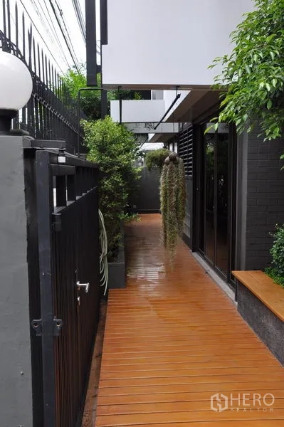 Detached House for rent in Watthana, Bangkok - Private side walkway with wooden deck, hanging plants and a secure black gate.