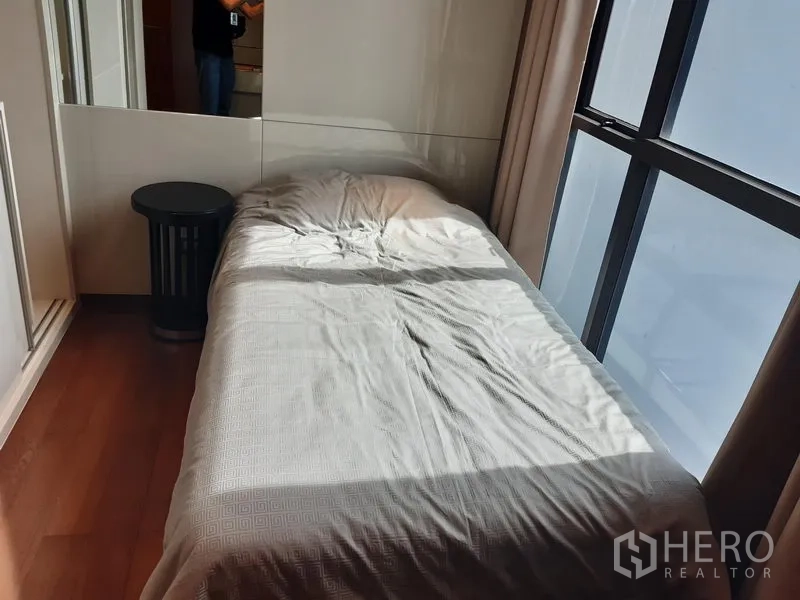 Condominium for rent in Khlong Toei, Bangkok - Sunlit single bedroom with wooden floor and tall window.