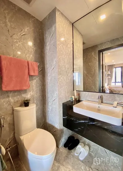Condominium for rent in Pathum Wan, Bangkok - Modern marble bathroom with large mirror, vanity and toilet.
