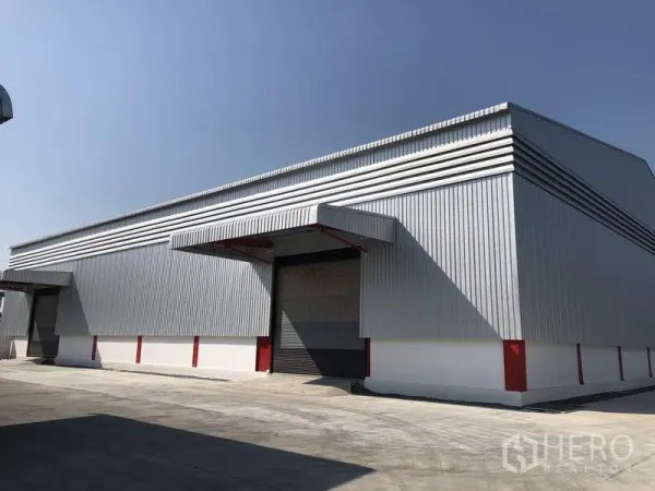 Warehouse for rent in Pak Kret, Nonthaburi - Modern metal-clad warehouse exterior with loading canopy and wide driveway in Pak Kret.
