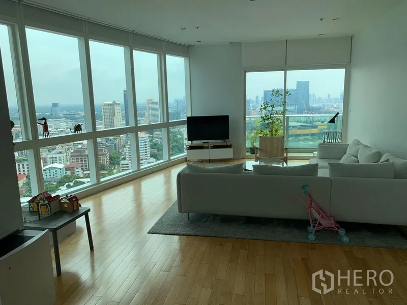 Condominium for rent in Khlong Toei, Bangkok - Corner living room with floor-to-ceiling windows, light wood floors, and panoramic Bangkok skyline views.