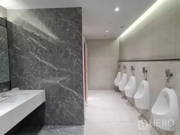 สำนักงาน ให้เช่า - ห้องน้ำชายสไตล์โมเดิร์น ผนังลายหินอ่อน เคาน์เตอร์ล้างมือยาว และโถปัสสาวะเรียงแถวในอาคารสำนักงาน