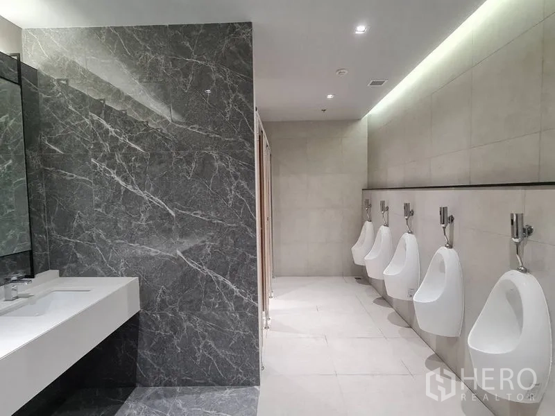 สำนักงาน ให้เช่า - ห้องน้ำชายสไตล์โมเดิร์น ผนังลายหินอ่อน เคาน์เตอร์ล้างมือยาว และโถปัสสาวะเรียงแถวในอาคารสำนักงาน