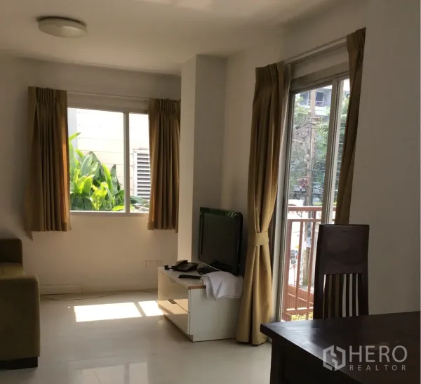 Condominium for sale in Pathum Wan, Bangkok - Bright living room in Pathum Wan condo with TV stand, sofa and balcony doors with beige curtains.