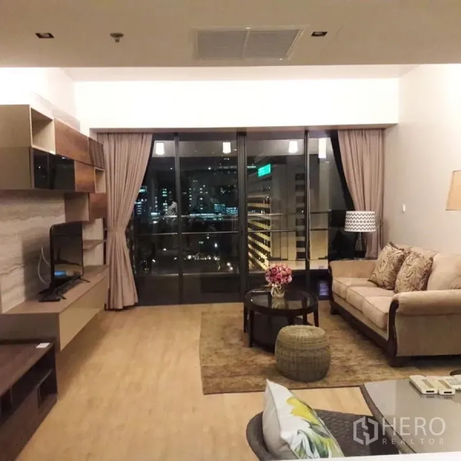 คอนโด ขายในSathon, Bangkok - ห้องนั่งเล่นยามค่ำ เปิดสู่ระเบียงเห็นทิวทัศน์ไฟเมืองและผนังทีวีบิลท์อิน