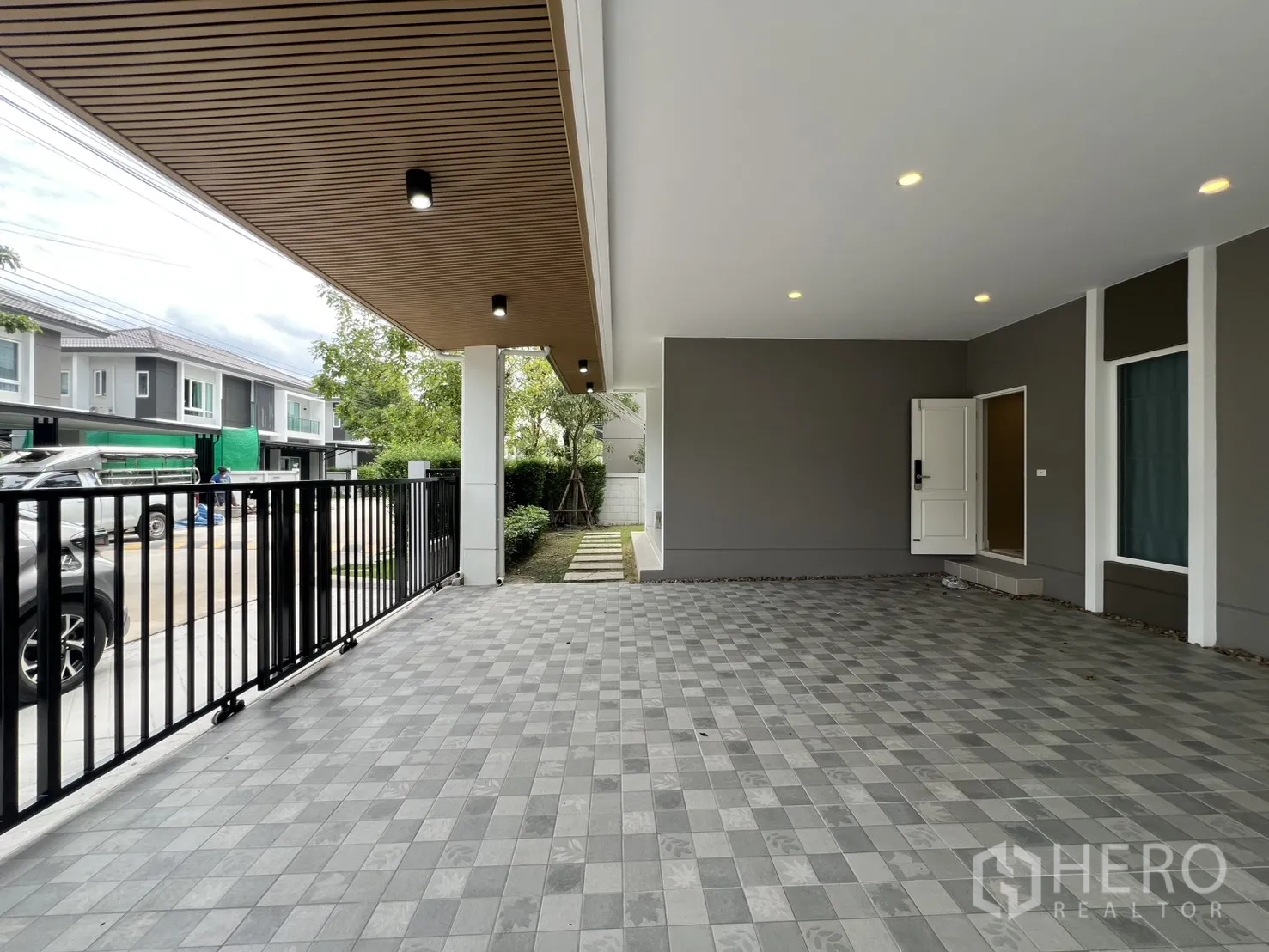 独栋房屋 for rent in Lat Krabang, Bangkok - 从车位望向街道的视角，黑色金属滑门与天花筒灯清晰可见。