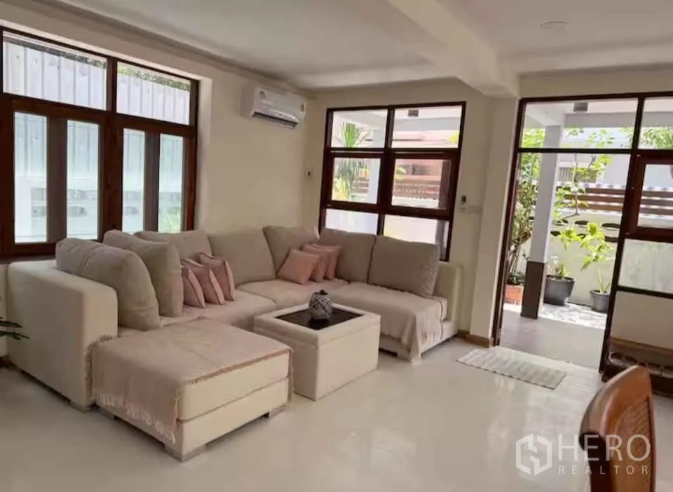 独立式住宅 出租在Khlong Toei, Bangkok - 明亮客厅，米色转角沙发，大窗与通往露台花园的门。