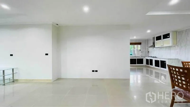 Detached House for rent in Bang Kapi, Bangkok - Open-plan living and dining area leading to a bright L-shaped kitchen with marble-look walls.