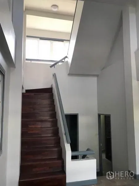 Townhouse for rent in Suan Luang, Bangkok - Staircase with dark wooden steps leading to a high ceiling and clerestory windows.