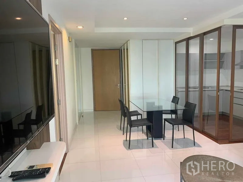 Condominium for rent or sale in Khlong Toei, Bangkok - Dining area with four chairs in front of the kitchen behind glass panels.