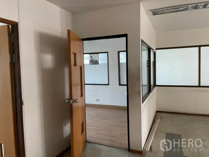 Warehouse for rent in Prawet, Bangkok - Small office corridor with a wood door, interior windows, and mixed flooring.