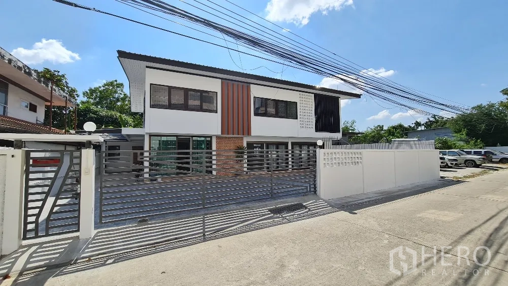 Detached House for rent in Lat Phrao, Bangkok - Front facade with sliding metal gate, paved driveway and parking area.