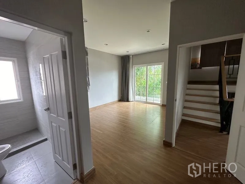 Detached House for sale in Bang Khen, Bangkok - Hallway with bathroom entrance, wood floors, and sliding doors to a balcony or garden.