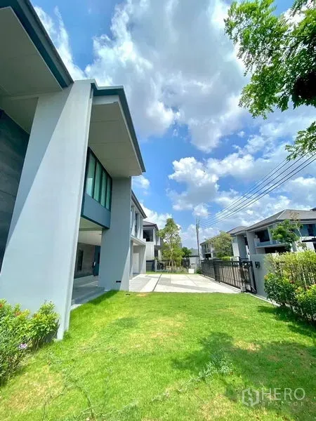Detached House for sale in Bang Kapi, Bangkok - Sunny front lawn beside a modern two-storey detached house with driveway and boundary fence.