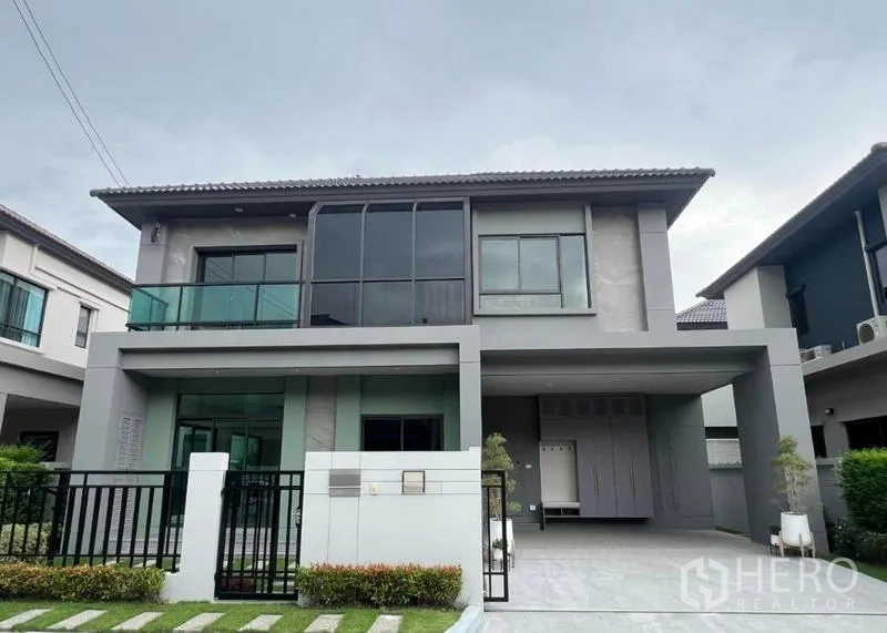 Detached House for sale in Bang Kruai, Nonthaburi - Modern two-storey detached house with glass balcony, gated front yard and a covered two-car carport.