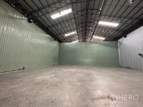 Warehouse for rent in Pak Kret, Nonthaburi - Wide open storage bay with corrugated metal walls, overhead lights and solid concrete slab.