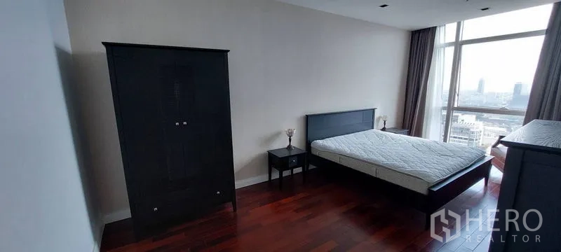 公寓 出租在Pathum Wan, Bangkok - 曼谷帕吞旺公寓的宽敞卧室，深色木地板，大窗户城市景观，黑色床与衣柜。