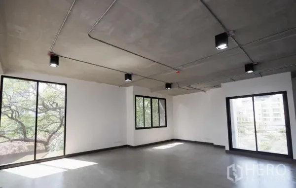办公空间 出租在Watthana, Bangkok - 明亮的开放式通罗办公室，大片窗户与绿景，抛光水泥地面与外露天花灯具。