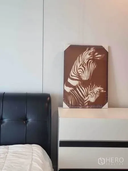 公寓 出租在Ratchathewi, Bangkok - 卧室一角，黑色皮质床头、白色斗柜与斑马装饰画。
