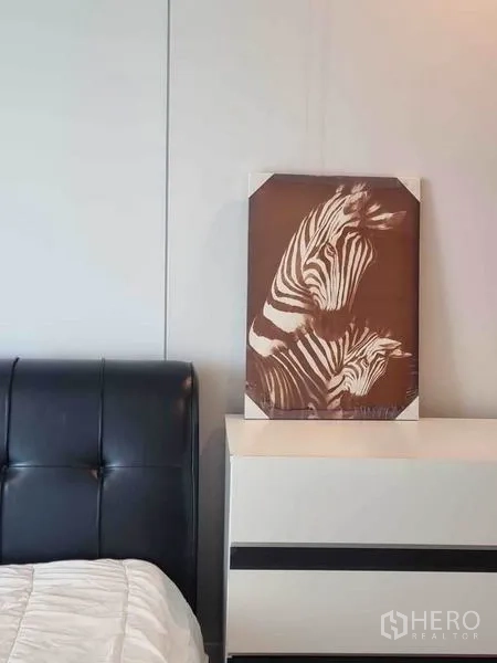 公寓 出租在Ratchathewi, Bangkok - 卧室一角，黑色皮质床头、白色斗柜与斑马装饰画。