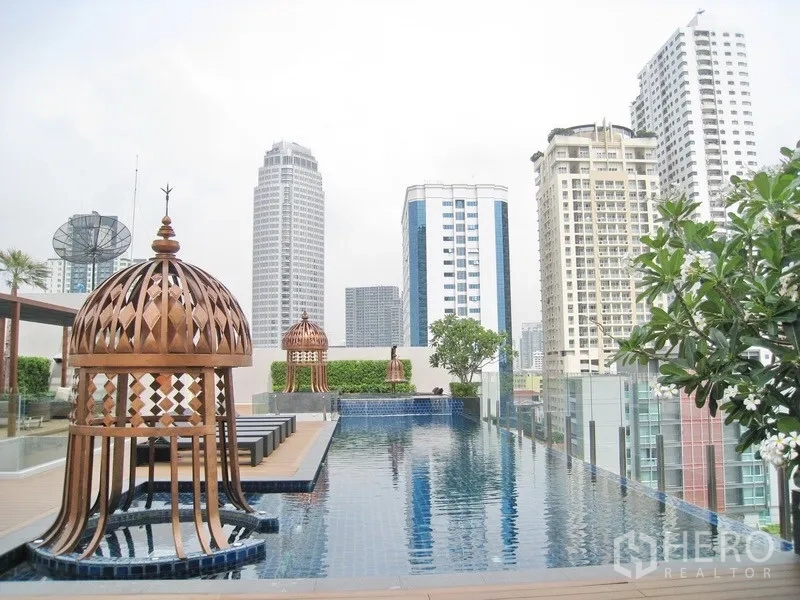 公寓 出租在Watthana, Bangkok - 屋顶泳池俯瞰城市天际线，木质平台、躺椅与装饰性凉亭。