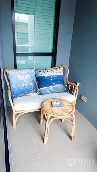 Townhouse for rent or sale in Suan Luang, Bangkok - Private balcony nook with a rattan bench and side table by the glass door.