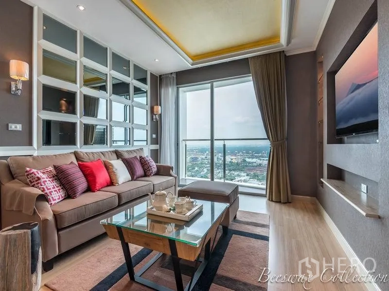 Condominium for rent in Watthana, Bangkok - Living room with floor‑to‑ceiling sliding doors to a balcony and panoramic Bangkok skyline view, plus sofa and TV wall.