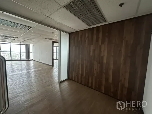 办公空间 出租在Watthana, Bangkok - 开放式办公区一角，木纹地板、木质特色墙与玻璃隔间，落地窗可见城市景观。