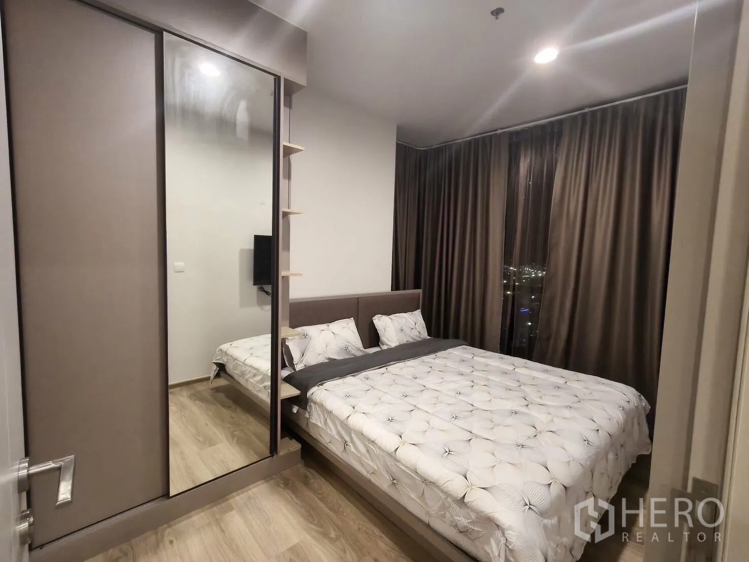 Condominium for rent in Khlong Toei, Bangkok - Master bedroom angle showing a large mirrored wardrobe and a floor-to-ceiling window with night lights outside.