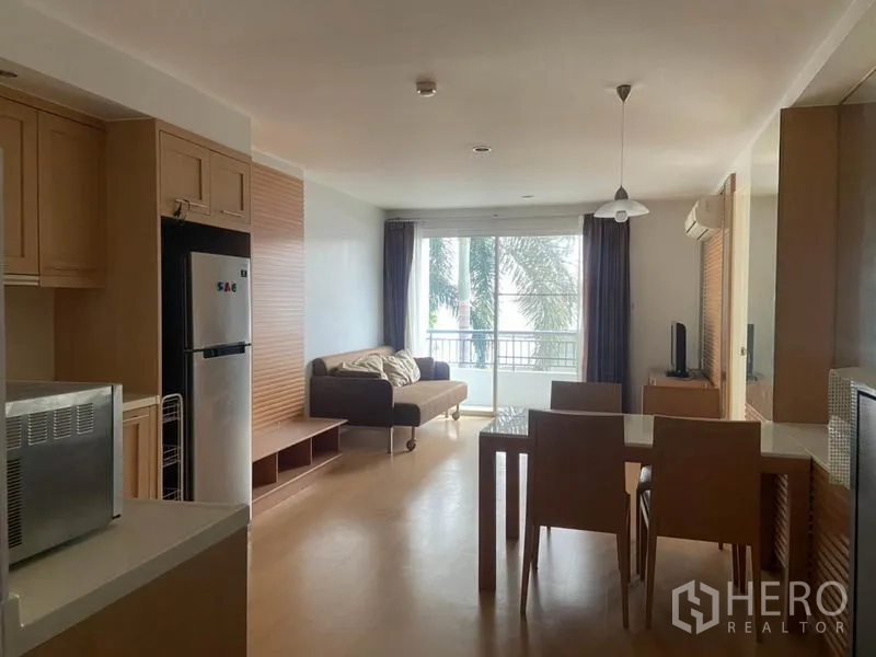 公寓 出租在Watthana, Bangkok - 从厨房望向起居区，可见餐桌、推拉玻璃门以及窗外绿景。