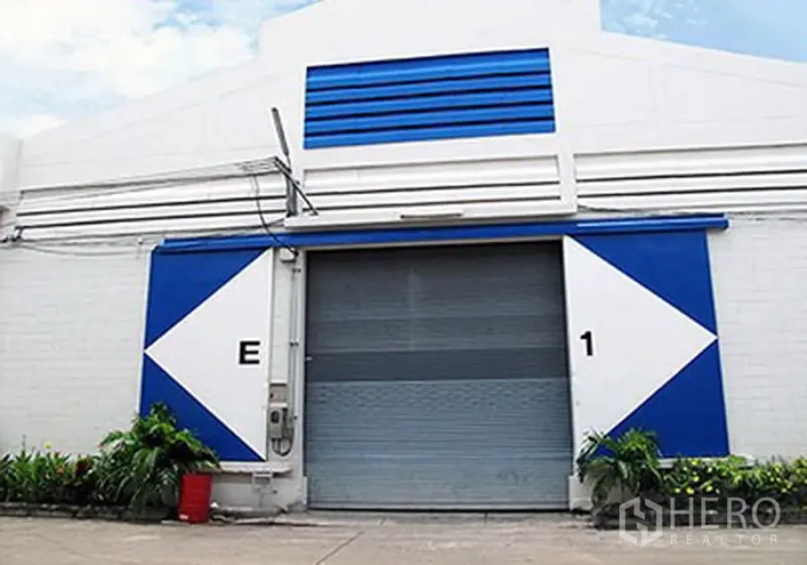 Warehouse for rent in Prawet, Bangkok - Industrial warehouse facade with blue-and-white panels and a large roller shutter door.