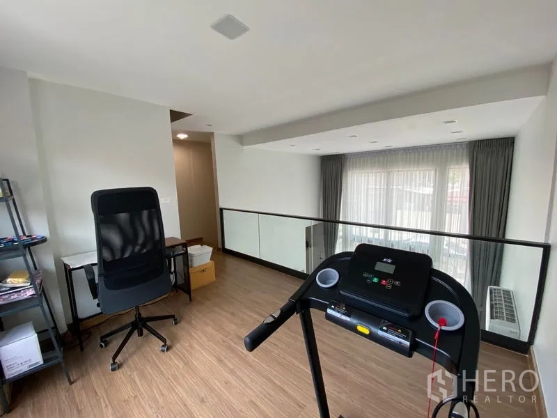 Townhouse for rent in Suan Luang, Bangkok - Mezzanine home office and fitness corner with treadmill, desk and glass balustrade.