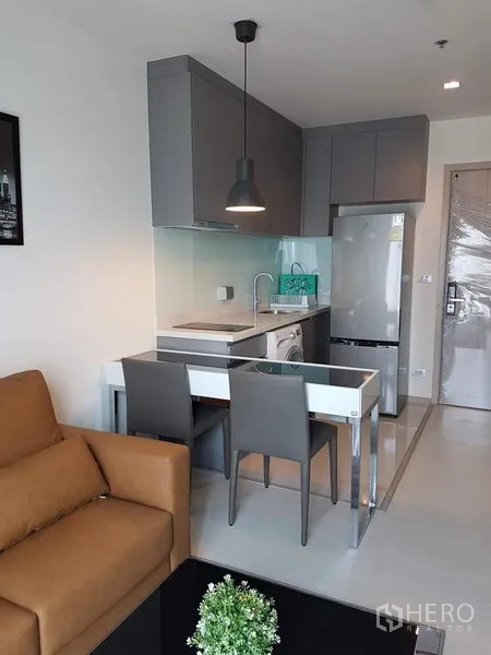 公寓 出租在Khlong Toei, Bangkok - 开放式小厨房，灰色橱柜、吊灯、餐桌、冰箱和洗衣机。