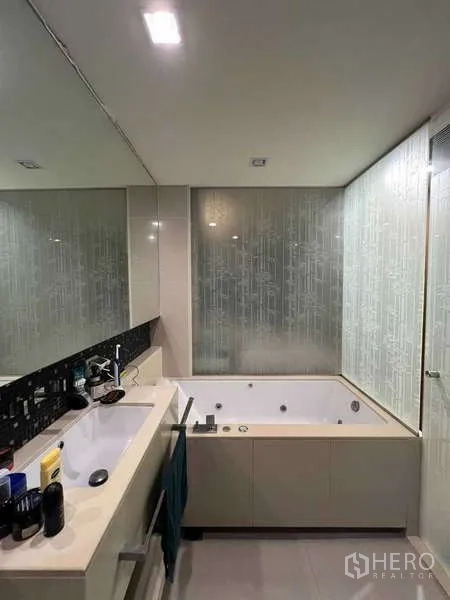 Condominium for rent in Bang Rak, Bangkok - Bathroom with vanity sink and jetted bathtub beside frosted glass.