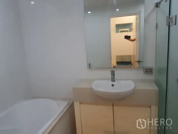 Condominium for rent in Khlong Toei, Bangkok - Clean bathroom with white vanity, large mirror and a built-in bathtub.