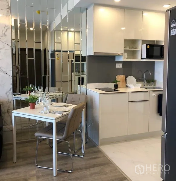 Condominium for rent in Bang Na, Bangkok - Bright kitchen with white cabinetry, induction hob and a small dining area.