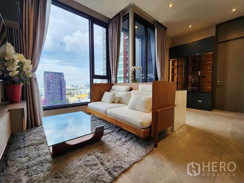 คอนโด ให้เช่าในWatthana, Bangkok - ห้องนั่งเล่นมุมกระจก เพดานสูง โซฟาไม้และโต๊ะกลางกระจก รับแสงธรรมชาติ