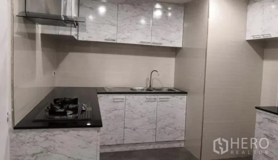 Condominium for rent in Khlong Toei, Bangkok - Built-in kitchen with marble-effect cabinets, black countertops, gas hob and stainless range hood.
