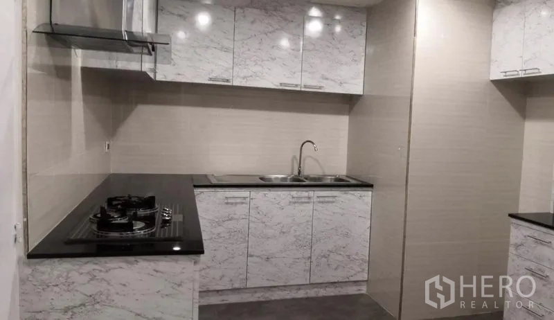 Condominium for rent in Khlong Toei, Bangkok - Built-in kitchen with marble-effect cabinets, black countertops, gas hob and stainless range hood.
