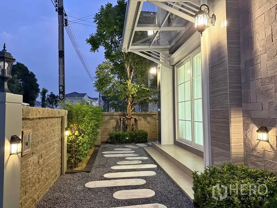 Semi-detached House for rent in Mueang Samut Prakan, Samut Prakan - Evening view of the front walkway with garden lighting and an awning.