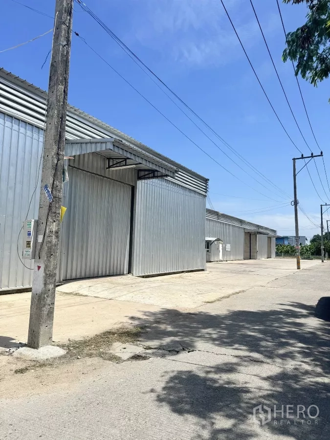 Warehouse for rent in Bang Lamung, Chon Buri - Multiple warehouse bays along a wide concrete road with easy truck access and utility poles.